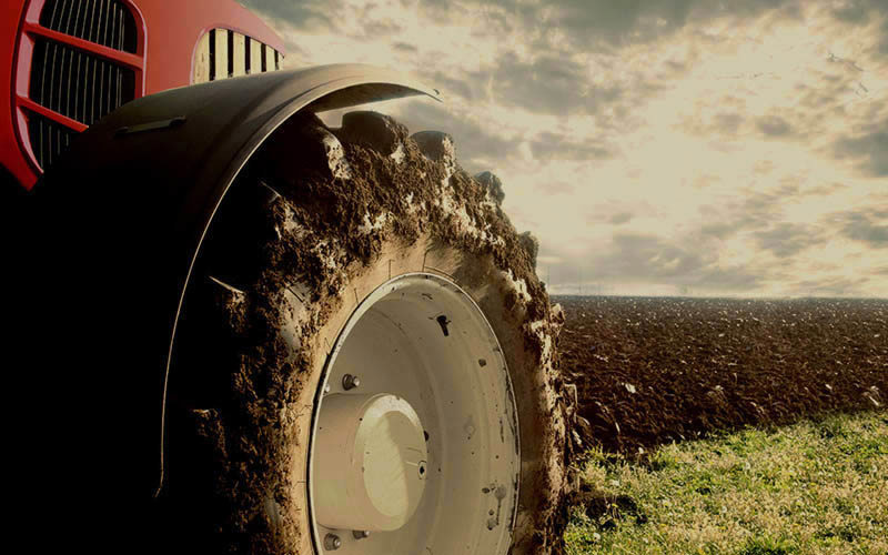 Tractor ploegt veld, toont robuuste banden en grondbewerking, ter voorbereiding op magazijnbouw. 